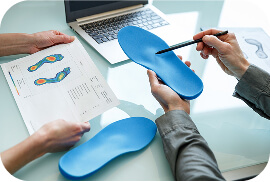 Due persone discutono su un plantare blu, mentre esaminano un grafico relativo all'analisi del piede, con un laptop aperto sul tavolo.