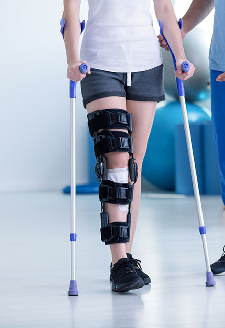 Una persona in piedi, che utilizza delle stampelle, indossa un tutore per il ginocchio nero, evidenziando un recupero post infortunio.